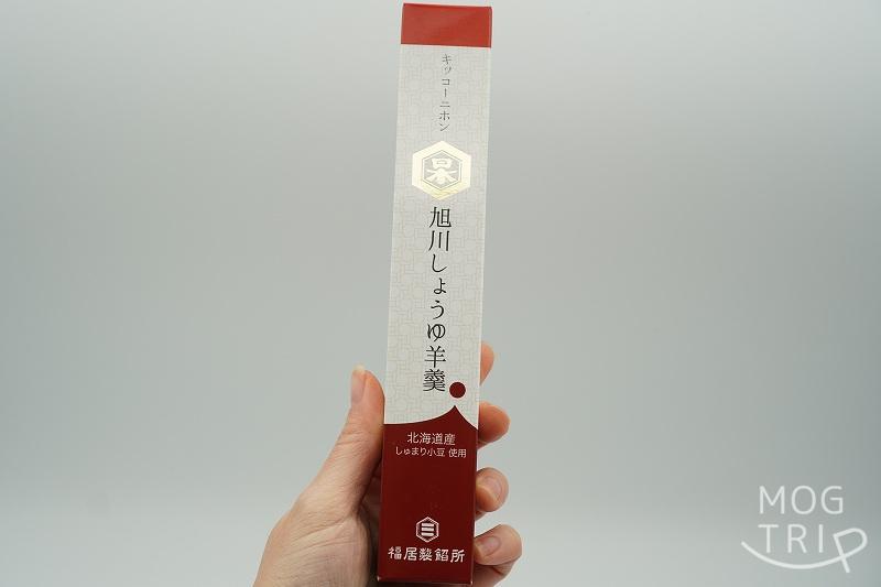 福居製餡所×キッコーニホンのコラボ商品「旭川しょうゆ羊羹」の箱を手に持っている様子