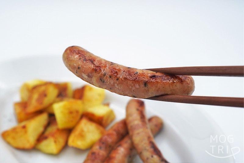 チキンじゅーしぃウインナー｜食創造さんだかん　箸でウインナーを持ち上げた様子